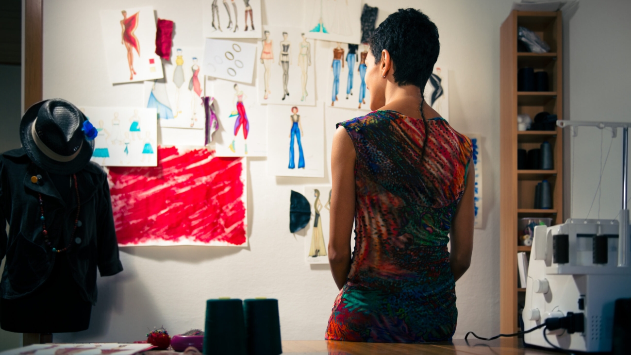 Young people and small business, hispanic woman at work as fashion designer and tailor, looking at sketches of new collection in atelier